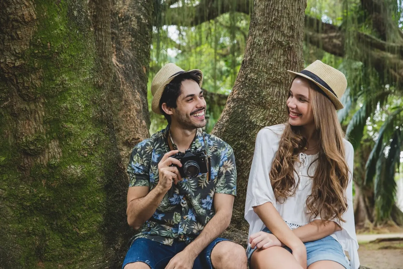 A smiling couple sits on a tree root.