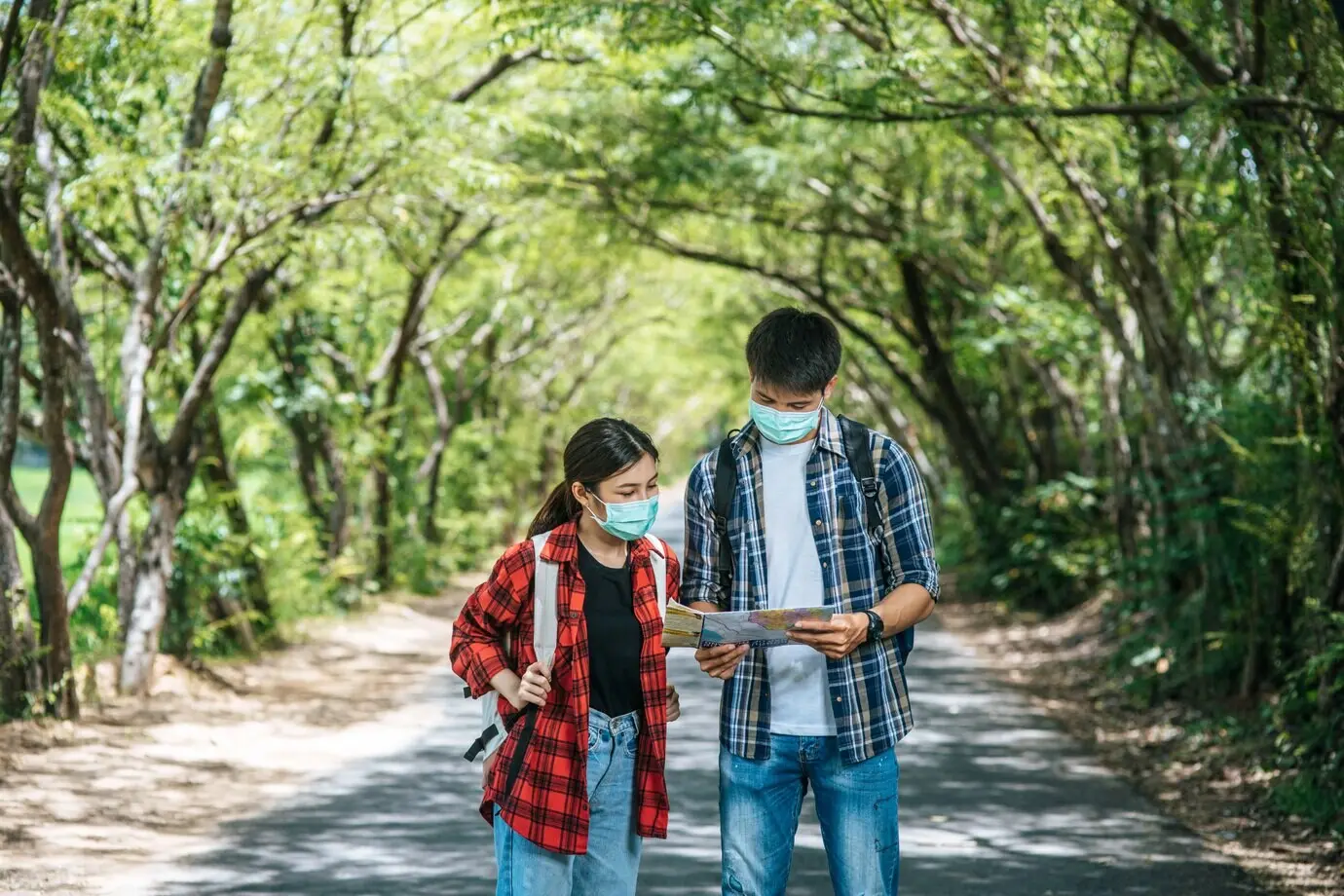 A male and a female tourist are wearing medical masks and looking at a map on the street.